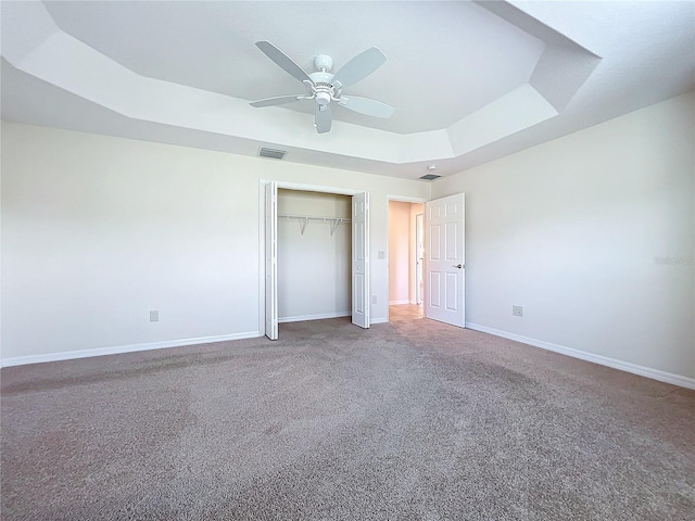 unfurnished bedroom featuring visible vents, baseboards, a closet, a tray ceiling, and carpet