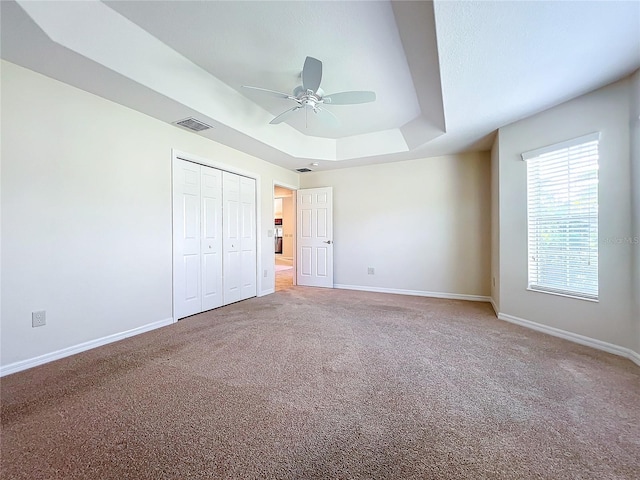 unfurnished bedroom featuring carpet floors, baseboards, visible vents, and a raised ceiling