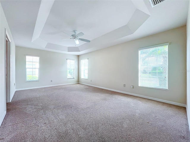 carpeted spare room with baseboards, visible vents, a tray ceiling, and a ceiling fan