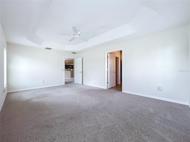 carpeted empty room with baseboards, visible vents, a tray ceiling, and ceiling fan