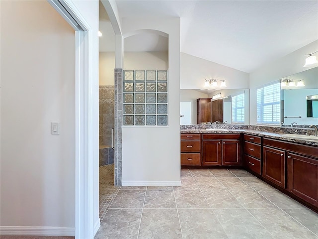 full bath featuring double vanity, tiled shower, tile patterned floors, vaulted ceiling, and a sink