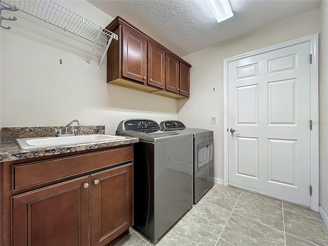 washroom featuring cabinet space, light tile patterned floors, a textured ceiling, separate washer and dryer, and a sink