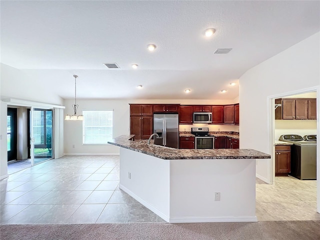 1338 Neuport Path, The Villages, FL 32163 - kitchen with stainless steel appliances, washing machine and dryer, dark brown cabinets, a spacious island, and dark stone countertops