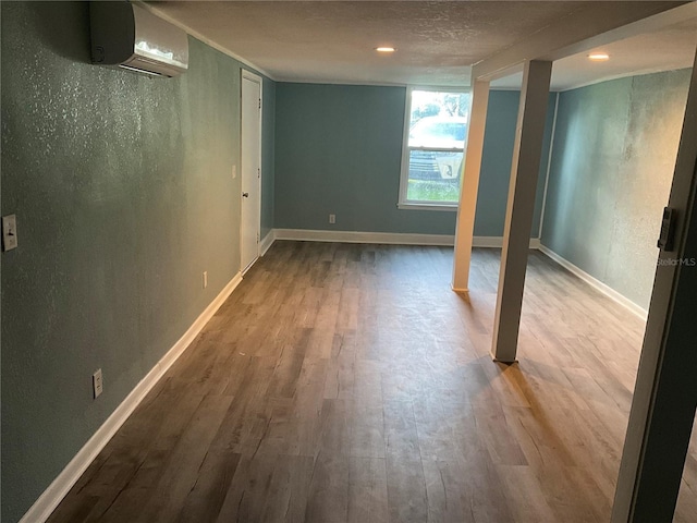 basement featuring wood-type flooring, a wall unit AC, and a textured ceiling