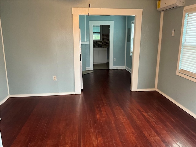 unfurnished room featuring a healthy amount of sunlight, a wall mounted air conditioner, and dark hardwood / wood-style floors