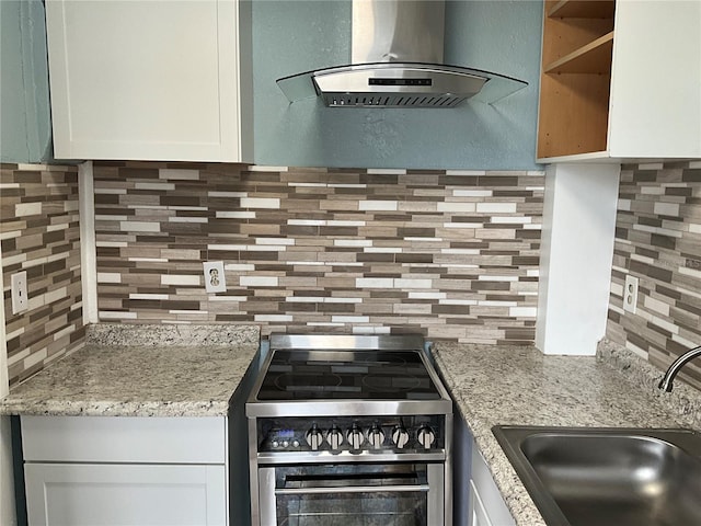 kitchen with light stone counters, high end stove, white cabinetry, sink, and exhaust hood