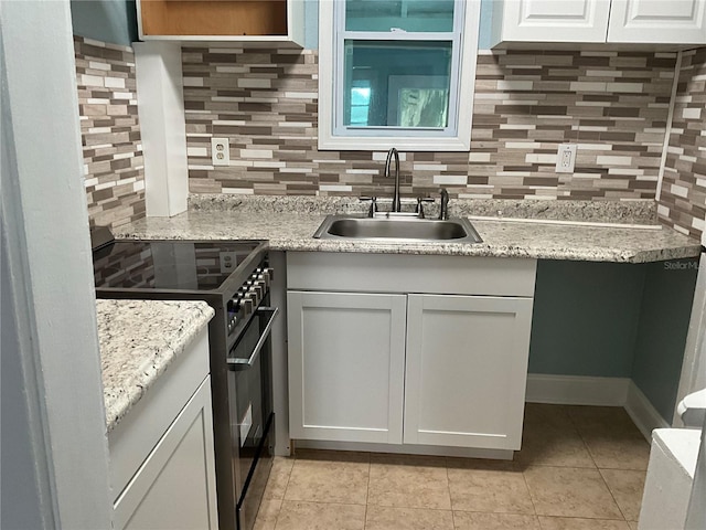 kitchen featuring backsplash, light tile patterned floors, gas stove, sink, and white cabinets