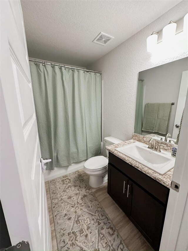 full bathroom featuring hardwood / wood-style flooring, vanity, shower / bath combination with curtain, a textured ceiling, and toilet