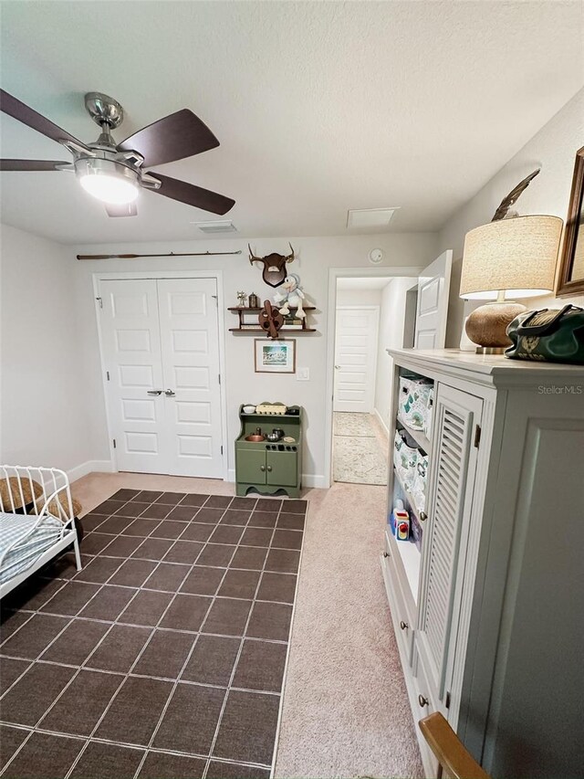 interior space featuring ceiling fan, a closet, a textured ceiling, and dark colored carpet