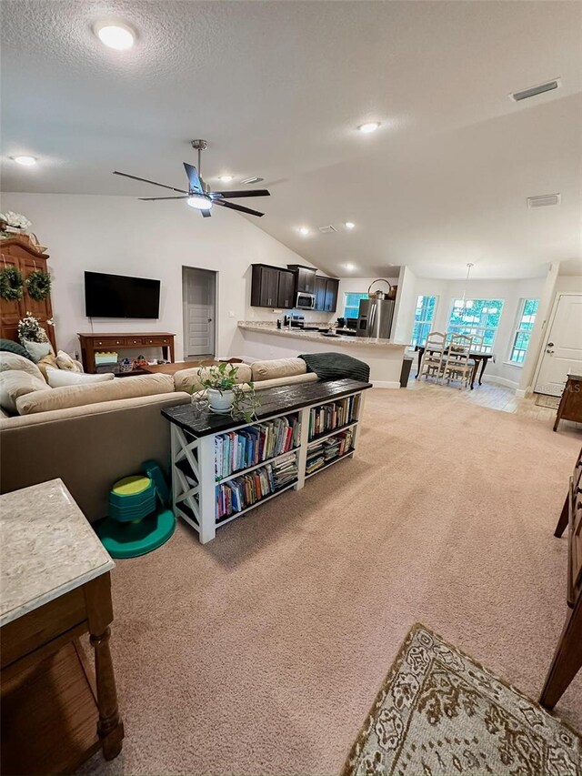 living room featuring lofted ceiling, light carpet, a textured ceiling, and ceiling fan