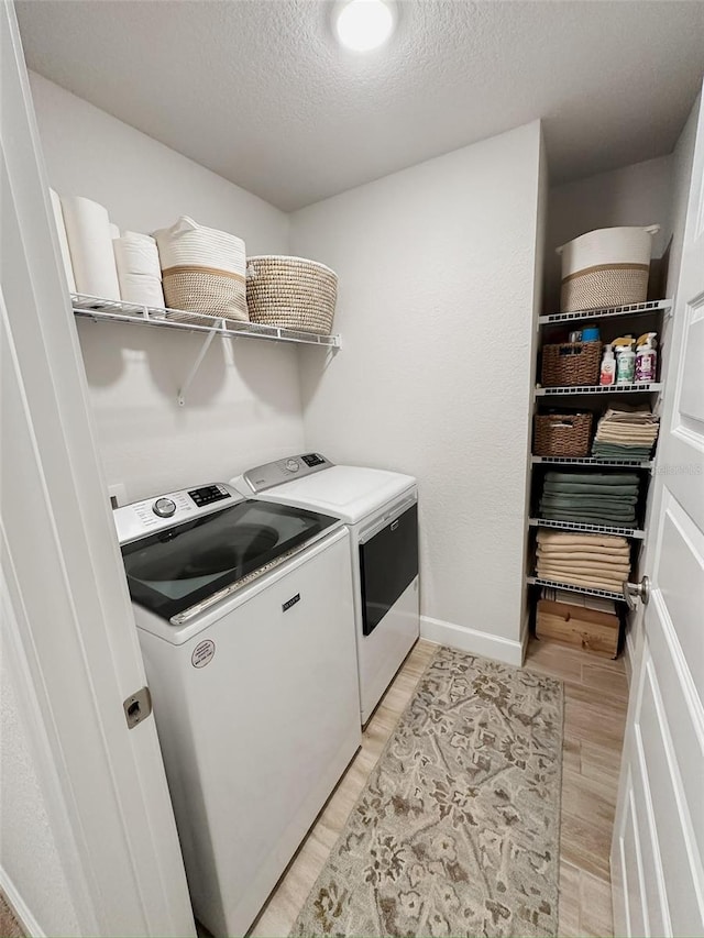 clothes washing area with washing machine and dryer, a textured ceiling, and light wood-type flooring