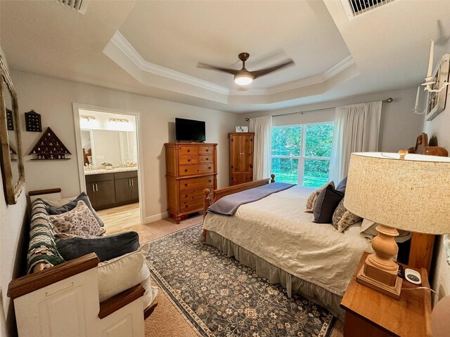 carpeted bedroom featuring crown molding, ensuite bath, a raised ceiling, and ceiling fan