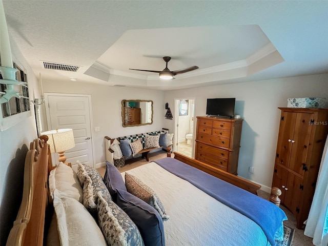 bedroom featuring ornamental molding, ensuite bath, ceiling fan, and a tray ceiling