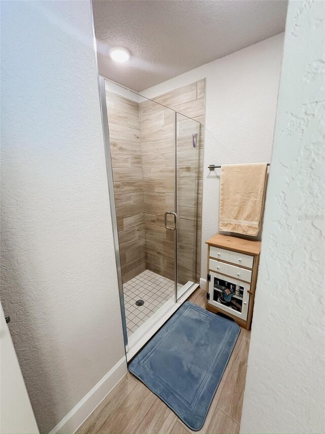 bathroom with hardwood / wood-style floors, an enclosed shower, and a textured ceiling