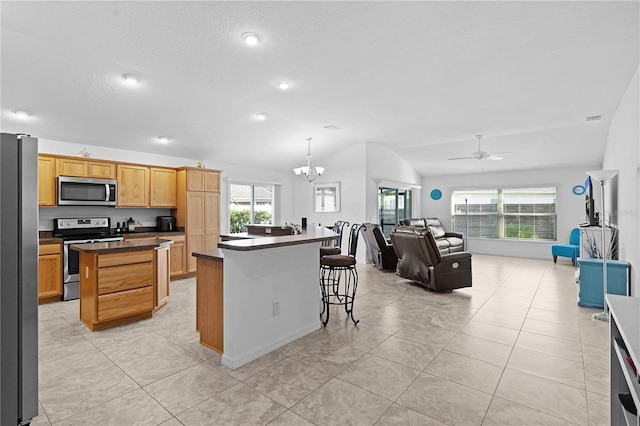 kitchen with appliances with stainless steel finishes, vaulted ceiling, ceiling fan with notable chandelier, and a center island