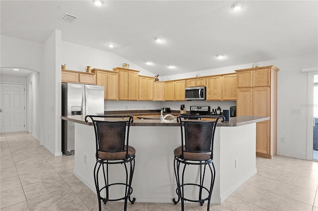 kitchen with a center island with sink, light tile patterned flooring, stainless steel appliances, vaulted ceiling, and a kitchen bar