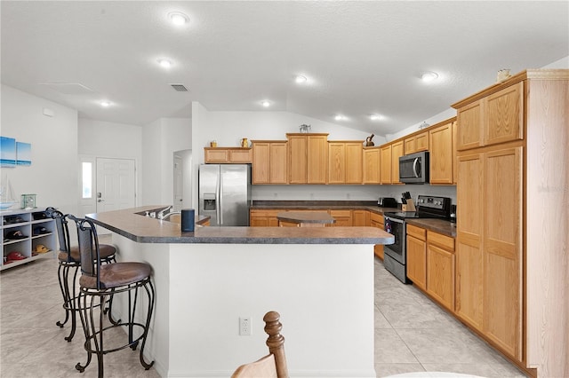 kitchen featuring a kitchen bar, light tile patterned floors, vaulted ceiling, an island with sink, and stainless steel appliances