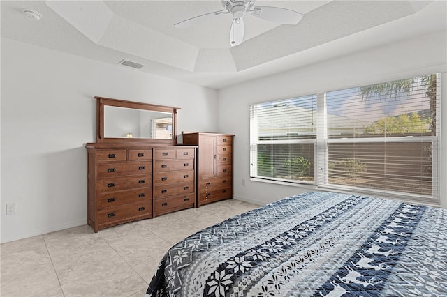 tiled bedroom with ceiling fan and a tray ceiling