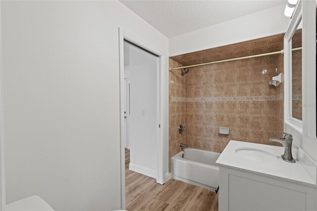 full bathroom featuring vanity, a textured ceiling, hardwood / wood-style flooring, toilet, and tiled shower / bath