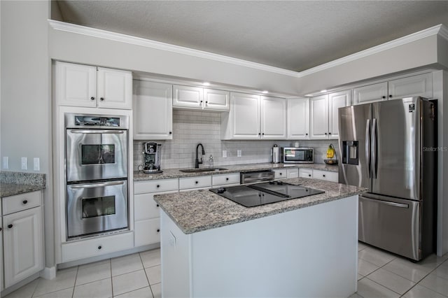 kitchen with appliances with stainless steel finishes, white cabinets, sink, light tile patterned floors, and a center island