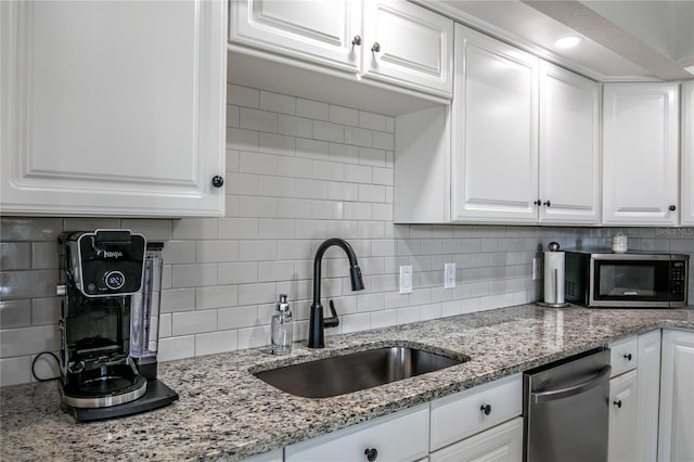 kitchen with appliances with stainless steel finishes, tasteful backsplash, white cabinetry, sink, and light stone countertops