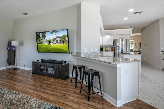 kitchen featuring white cabinets, light stone counters, kitchen peninsula, light wood-type flooring, and stainless steel fridge with ice dispenser