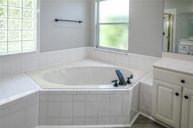 bathroom featuring tiled bath, a healthy amount of sunlight, and vanity