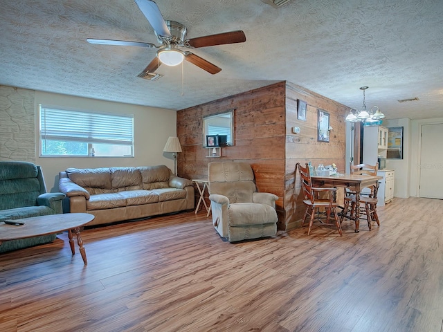 living room featuring ceiling fan with notable chandelier, light hardwood / wood-style flooring, and a textured ceiling