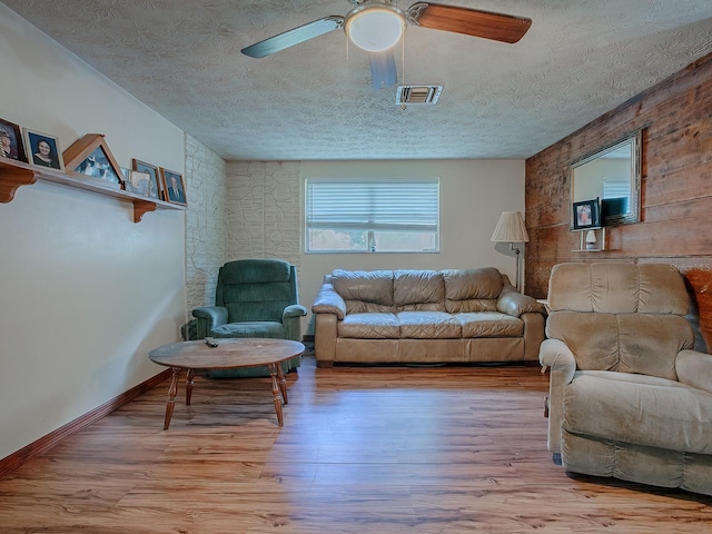 living room with a textured ceiling, ceiling fan, and light wood-type flooring