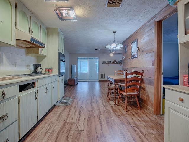 kitchen featuring hanging light fixtures, light hardwood / wood-style floors, decorative backsplash, a textured ceiling, and black oven