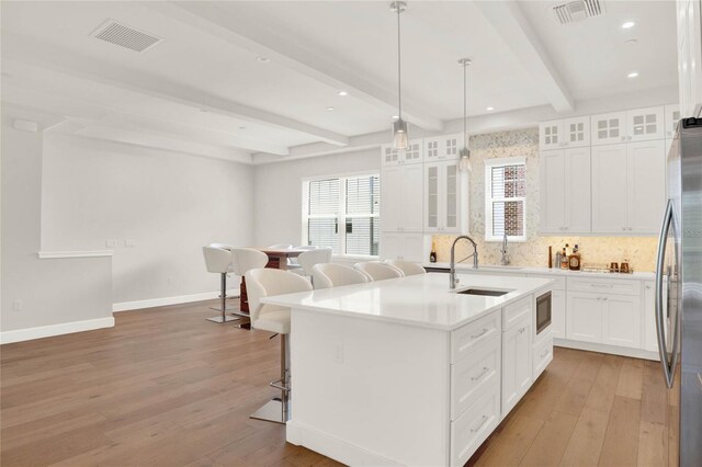 kitchen featuring beamed ceiling, light hardwood / wood-style floors, appliances with stainless steel finishes, and a center island with sink