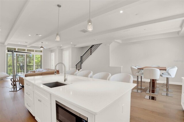 kitchen with sink, light hardwood / wood-style flooring, stainless steel microwave, and beam ceiling