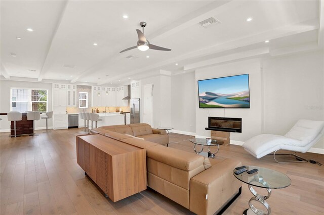 living room with beamed ceiling, light hardwood / wood-style flooring, and ceiling fan