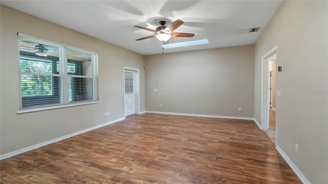 empty room featuring a skylight, ceiling fan, and hardwood / wood-style floors