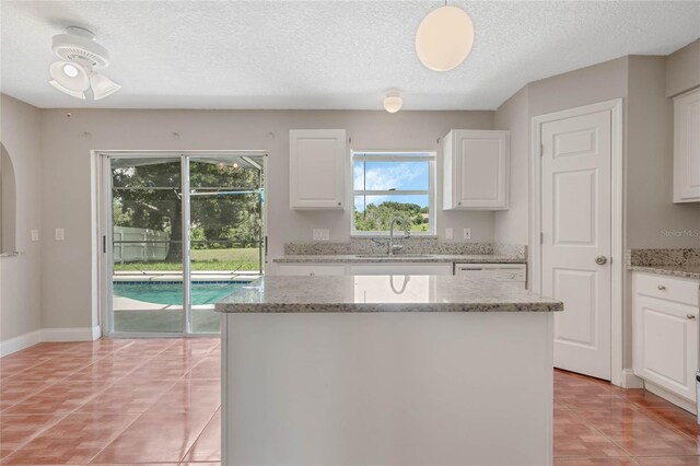 kitchen featuring white cabinetry, light tile patterned floors, a textured ceiling, a kitchen island, and sink