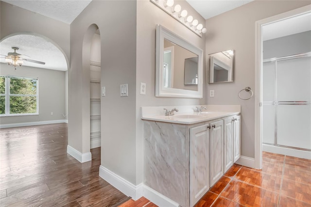 bathroom featuring a shower with shower door, wood-type flooring, a textured ceiling, vanity, and ceiling fan