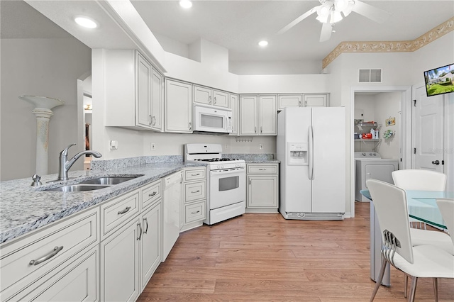 kitchen with sink, light stone counters, light hardwood / wood-style flooring, independent washer and dryer, and white appliances