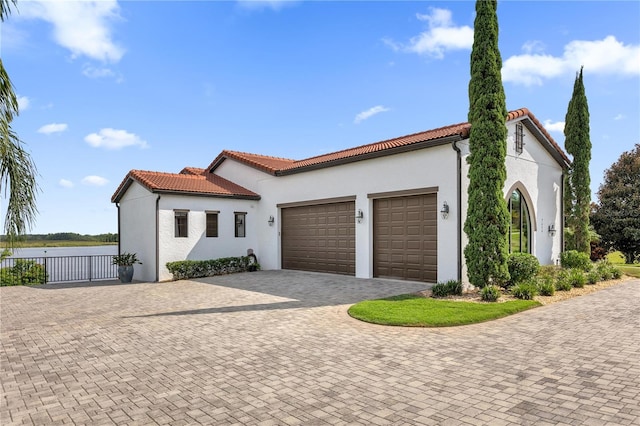 mediterranean / spanish-style home with a tiled roof, an attached garage, a water view, decorative driveway, and stucco siding