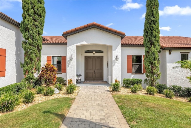 property entrance with a yard, a tiled roof, and stucco siding