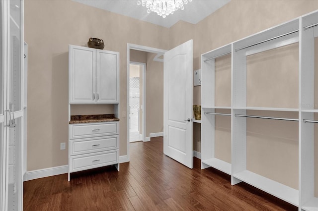 walk in closet with dark wood-style flooring and an inviting chandelier