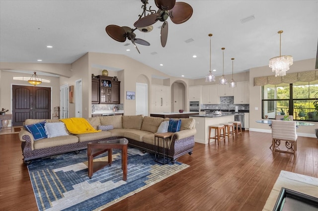 living area with visible vents, arched walkways, baseboards, dark wood-style floors, and ceiling fan with notable chandelier