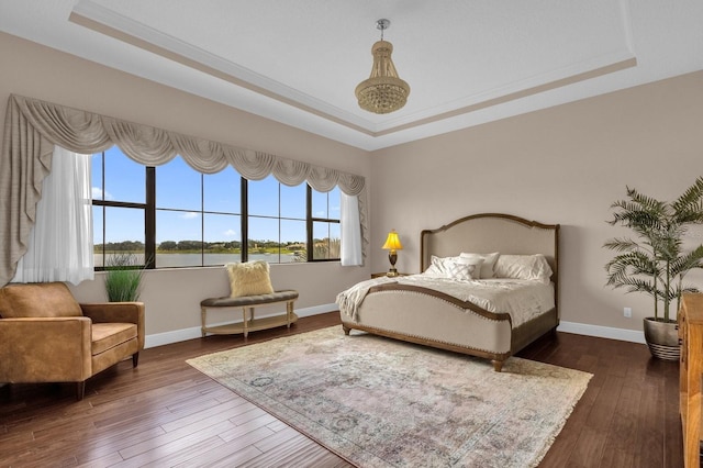 bedroom featuring a tray ceiling, dark wood-style flooring, and baseboards