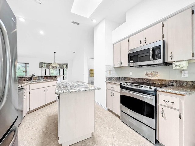 kitchen with tasteful backsplash, light tile patterned floors, a kitchen island, stainless steel appliances, and hanging light fixtures