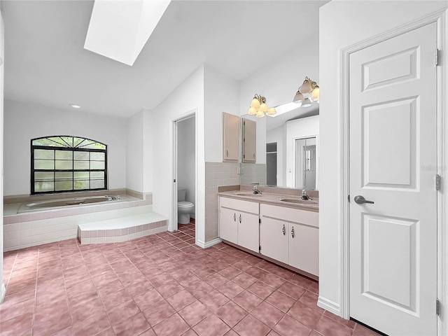 bathroom featuring double vanity, tile patterned flooring, toilet, vaulted ceiling with skylight, and a relaxing tiled tub