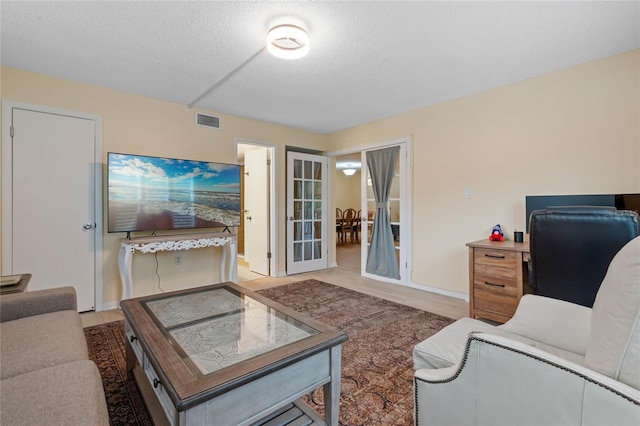 living room featuring french doors, a textured ceiling, and light wood-type flooring