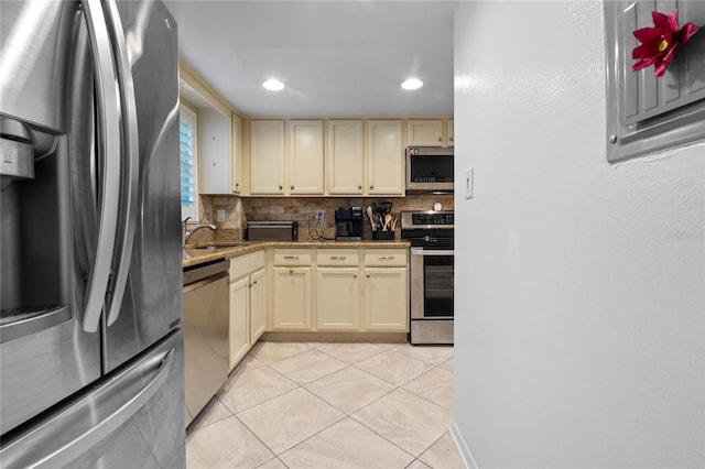 kitchen featuring appliances with stainless steel finishes, cream cabinets, light stone countertops, light tile patterned flooring, and decorative backsplash