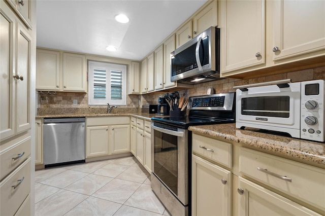 kitchen featuring light stone counters, light tile patterned floors, stainless steel appliances, cream cabinets, and decorative backsplash