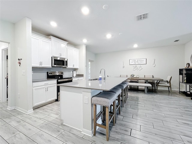 kitchen featuring white cabinets, sink, appliances with stainless steel finishes, and a center island with sink