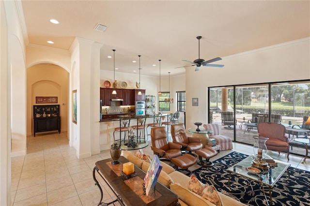 living room with ceiling fan, light tile patterned flooring, ornamental molding, and a towering ceiling