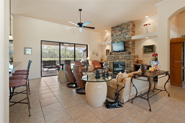 tiled living room featuring ceiling fan, a fireplace, a towering ceiling, and crown molding